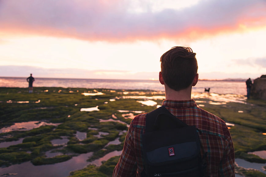 Man with Backpack Watching Sunset Over Mossy Coastline
