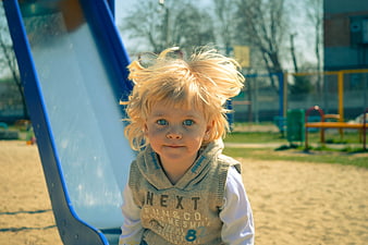 Blonde toddler boy with messy hair at outdoor playground