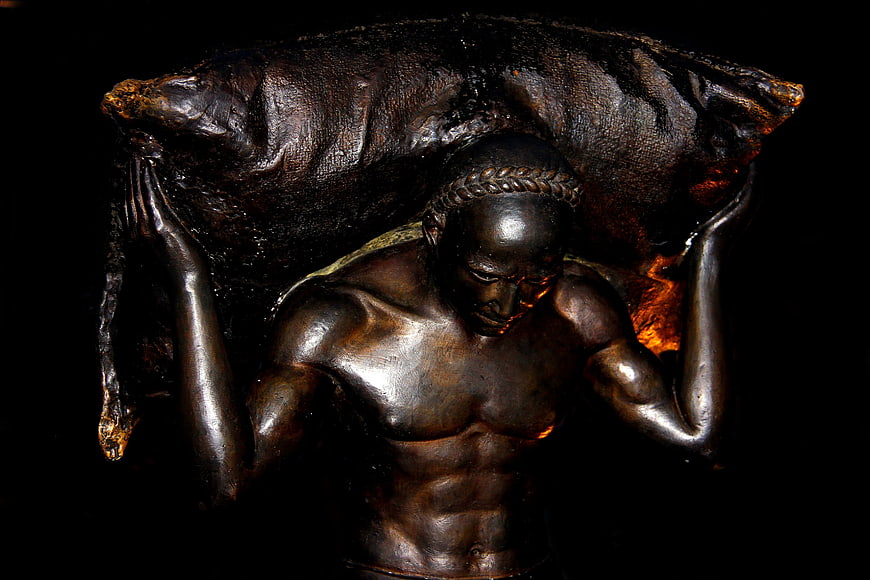 Bronze statue of a muscular man carrying a heavy sack on his shoulders