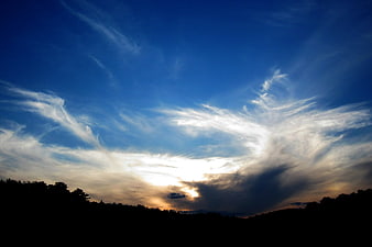 Dramatic sunset sky with wispy clouds over dark forest silhouette