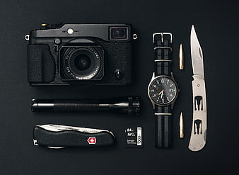Flat lay of vintage camera, watch, knife, and flashlight on black background
