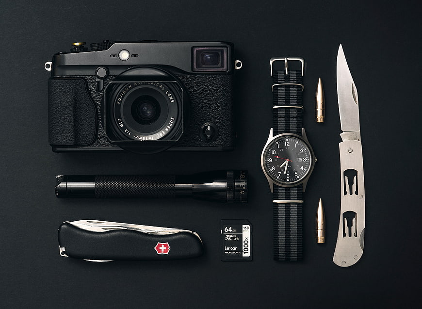 Flat lay of vintage camera, watch, knife, and flashlight on black background