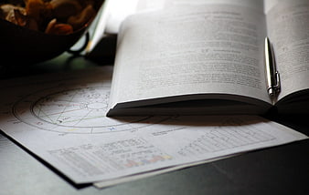 Open astrology book with zodiac chart and pen on desk