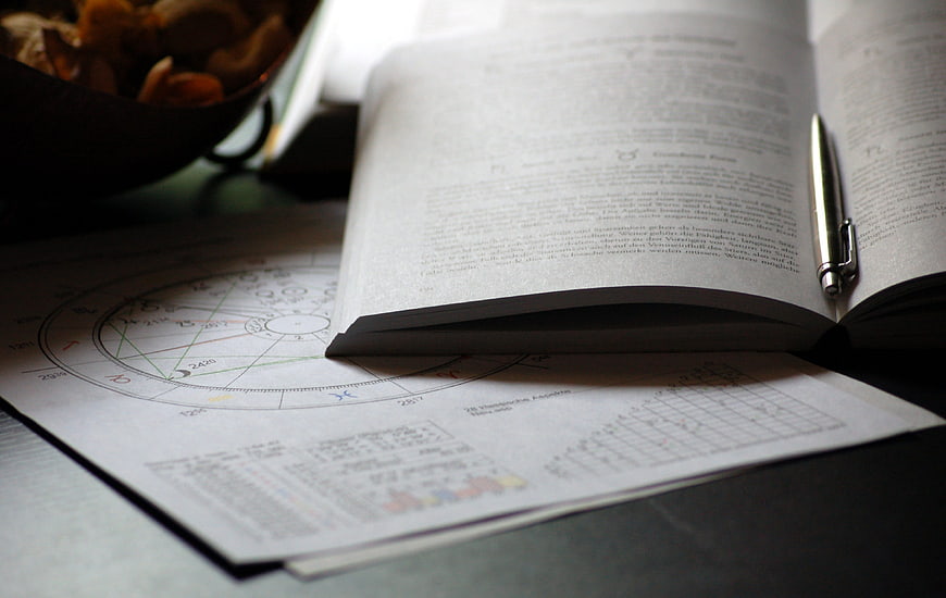 Open astrology book with zodiac chart and pen on desk