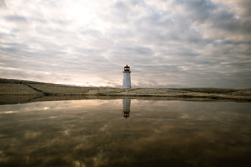 Lighthouse Reflection on Rocky Shore Under Cloudy Sky