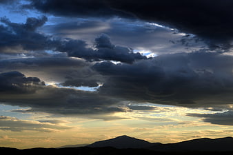 Dramatic sunset sky with dark clouds over mountain silhouette