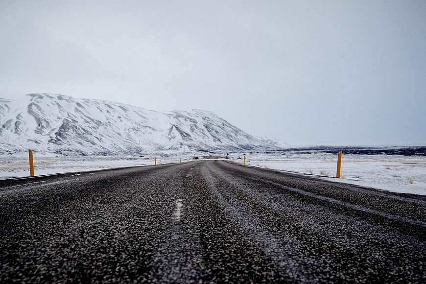 Wet asphalt road stretching through snowy winter landscape