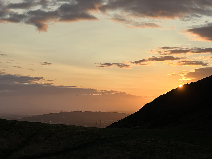 Sunset Silhouette Over Rolling Hills and Distant Cityscape