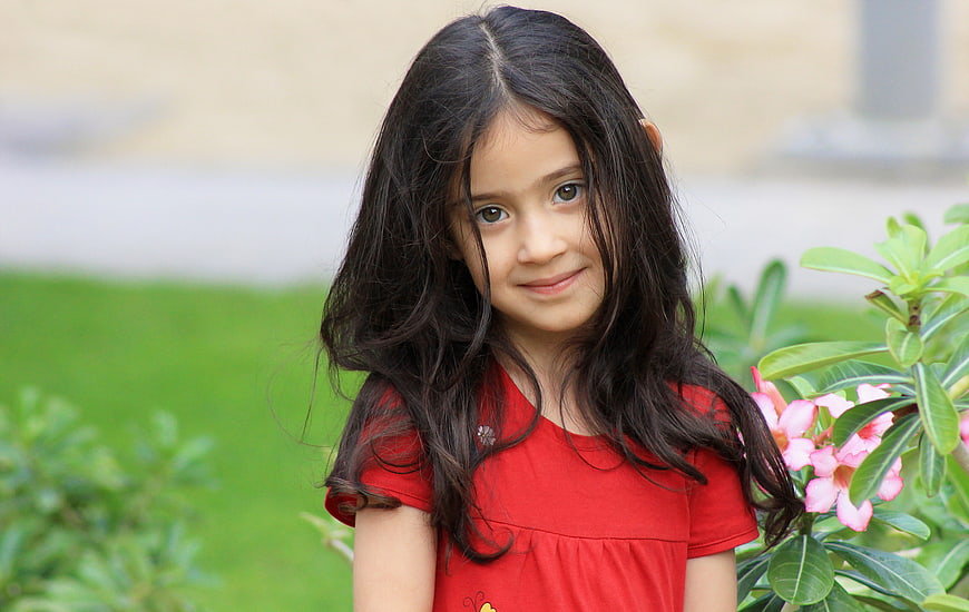 Cute little girl with long dark hair smiling in garden