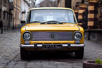 Front view of vintage yellow car on cobblestone street