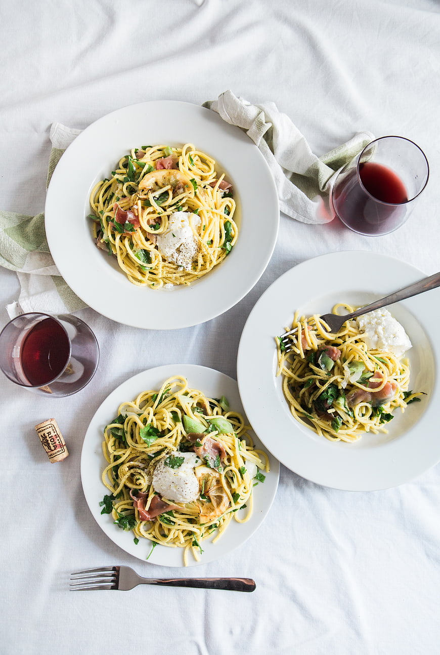 Overhead view of three plates of pasta with poached eggs and red wine