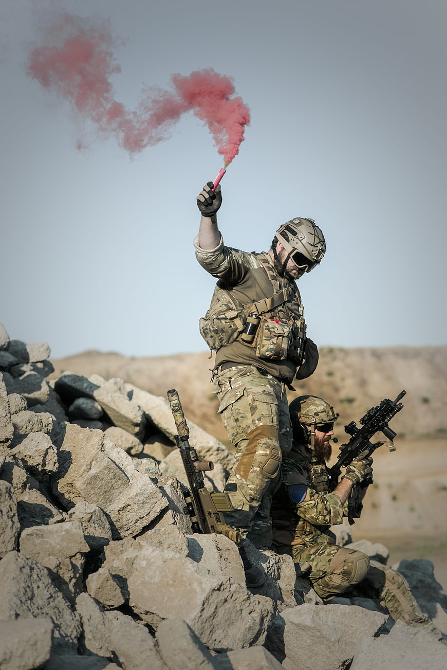 Soldiers with Guns on Rocks Holding Red Smoke Flare