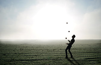 Silhouette of man juggling in vast open field