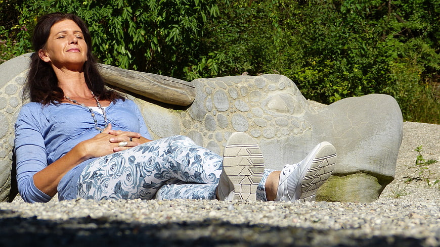 Woman relaxing on a stone dragon sculpture in a sunny garden
