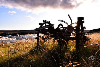 Rusty Farm Plow Silhouette in Grassy Field by River