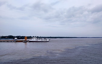White passenger ferry docked at river pier under cloudy sky