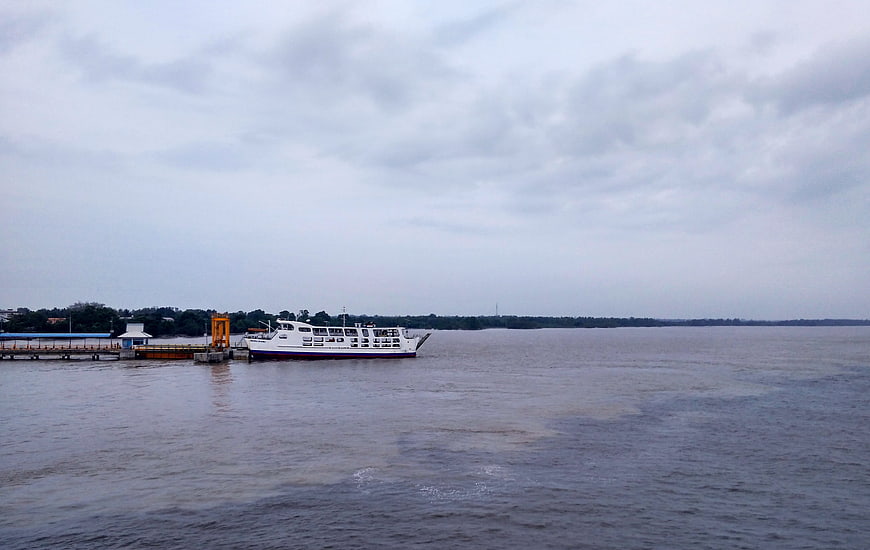 White passenger ferry docked at river pier under cloudy sky