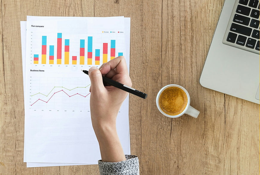 Hand Analyzing Business Financial Charts on Wooden Desk
