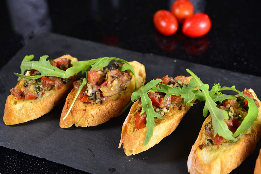 Gourmet Bruschetta Tapas With Arugula On Dark Slate Serving Board