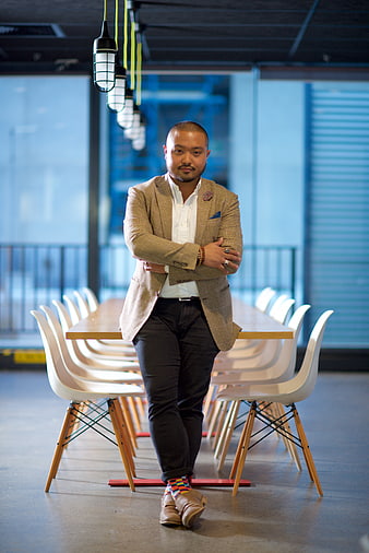 Confident Asian businessman in beige blazer leaning on conference table