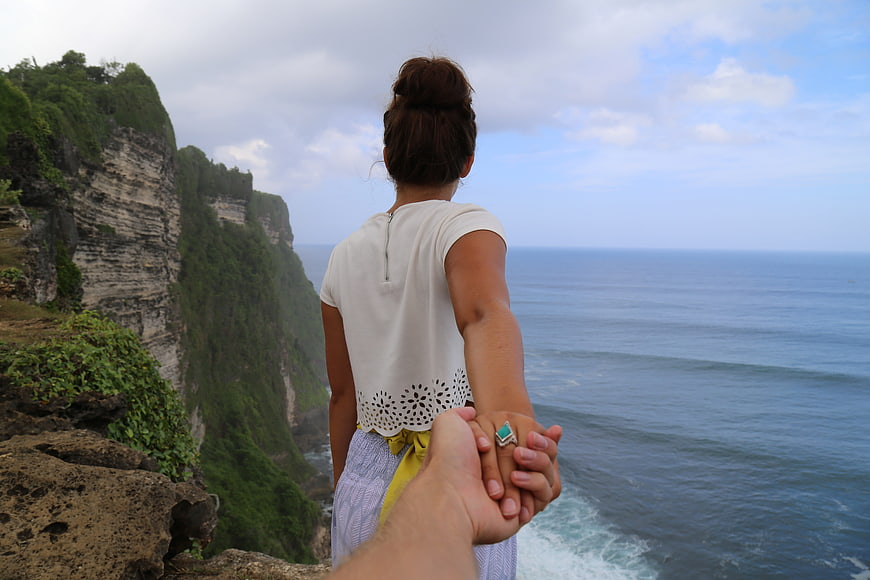 Couple holding hands overlooking ocean cliffs from behind