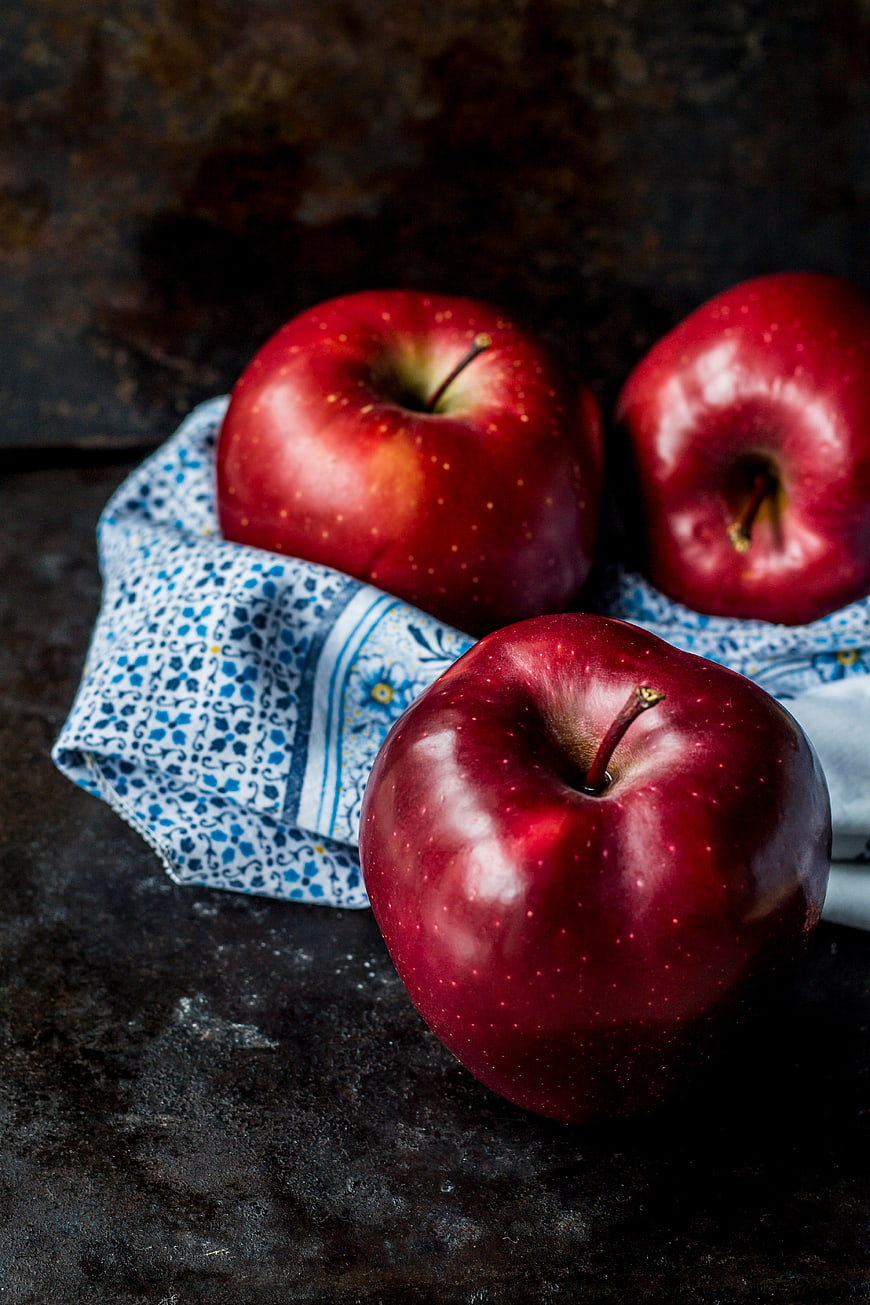 Three shiny red apples on a dark rustic background with blue cloth