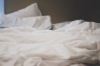 Unmade white bed with wrinkled sheets and pillows