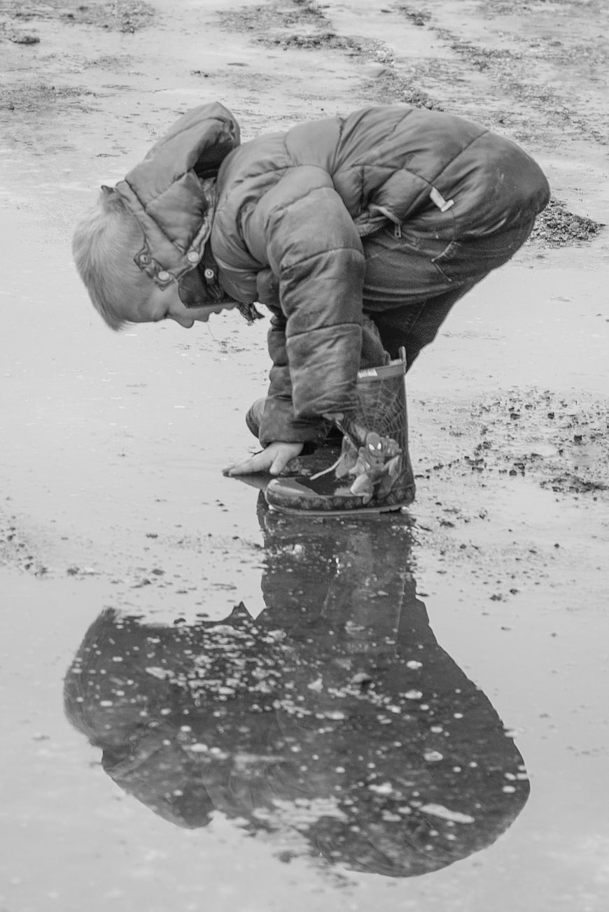 Child playing in a puddle with reflection in black and white