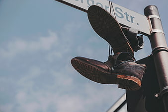 Vintage brown shoes hanging on street sign against blue sky