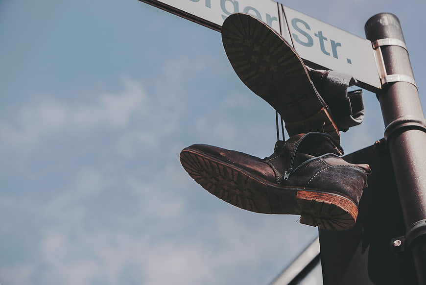 Vintage brown shoes hanging on street sign against blue sky