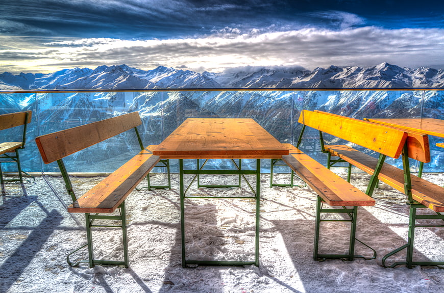 Wooden Tables and Benches on Snowy Alpine Terrace with Mountain View