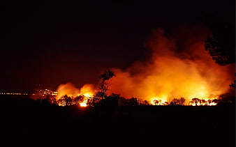 Massive wildfire burning at night with orange flames and smoke