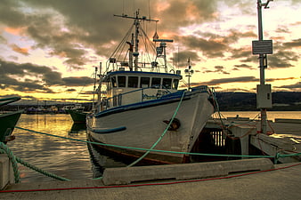 Fishing boat docked at harbor during golden hour sunset