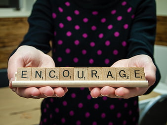 Hands holding wooden tiles spelling encourage
