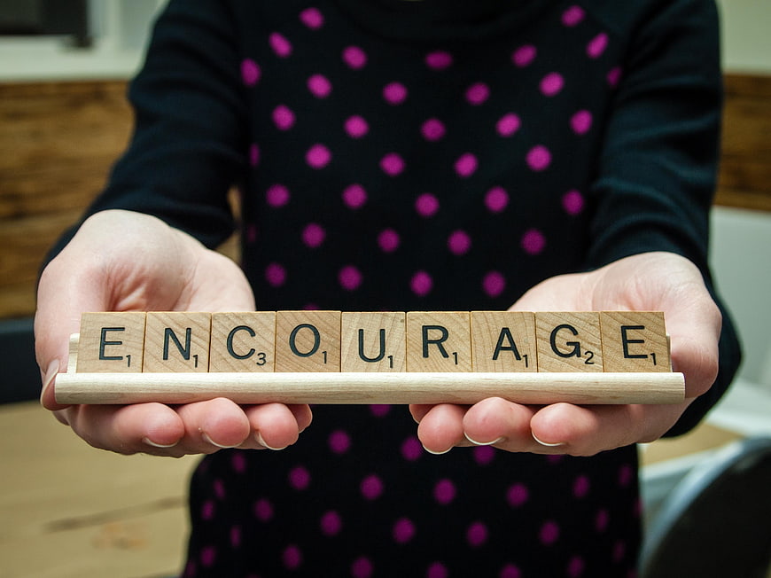 Hands holding wooden tiles spelling encourage