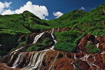 Lush Green Mountain Waterfall with Rust-Colored Rocks