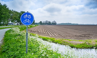 Blue bicycle path sign in rural agricultural landscape