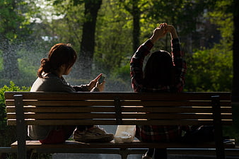 Two Women Relaxing on Park Bench with Smartphone