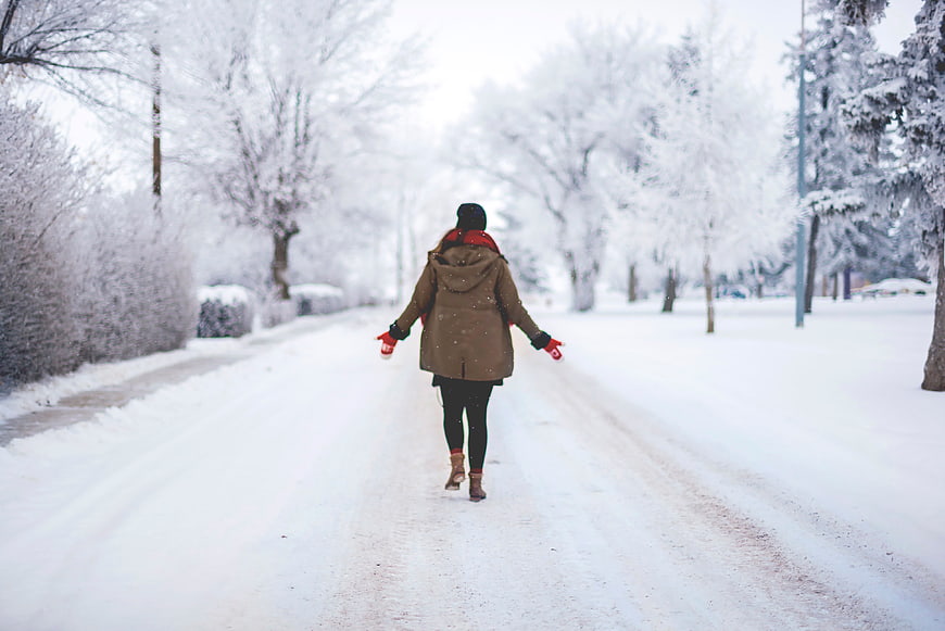 Woman walking down snowy winter road with red gloves
