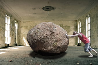 Young man pushing a giant boulder in an abandoned room