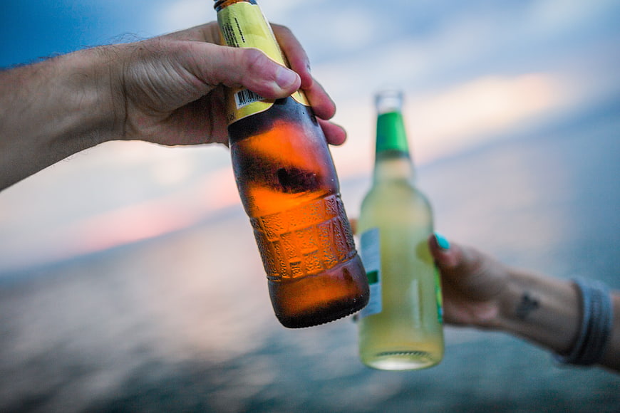 Friends toasting with beer bottles at sunset by the ocean
