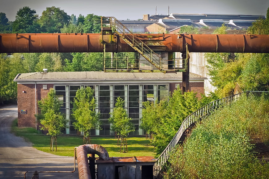Rusty industrial pipe over brick building with green trees