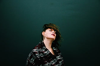 Woman with messy hair looking up against dark teal background