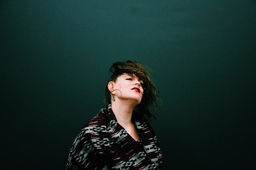 Woman with messy hair looking up against dark teal background