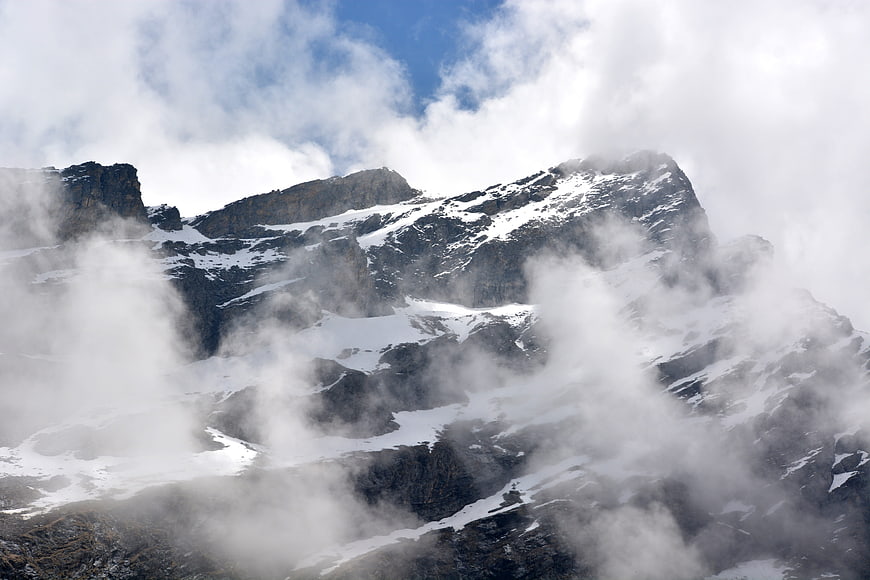 Snowy mountain peaks emerging through thick white clouds