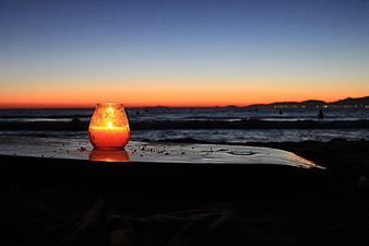 Glowing Candle on Beach at Sunset with Ocean Horizon