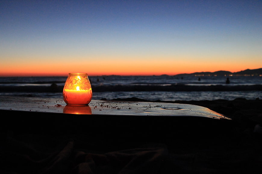Glowing Candle on Beach at Sunset with Ocean Horizon