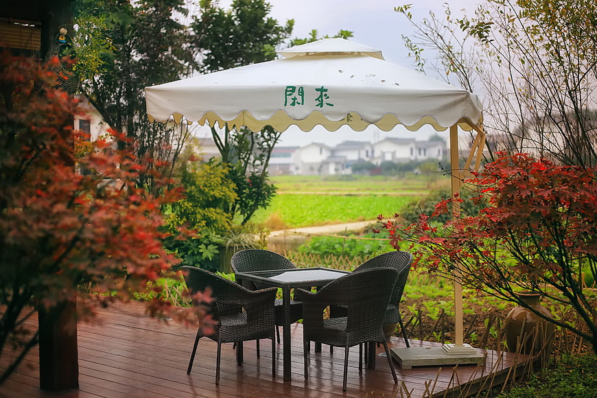 Rustic outdoor patio with white umbrella and red maple trees