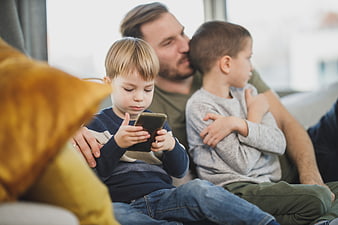 Father and Two Sons Relaxing on Couch with Smartphone