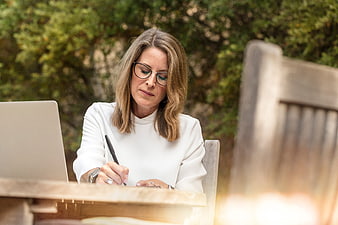 Professional woman writing notes at outdoor desk with laptop